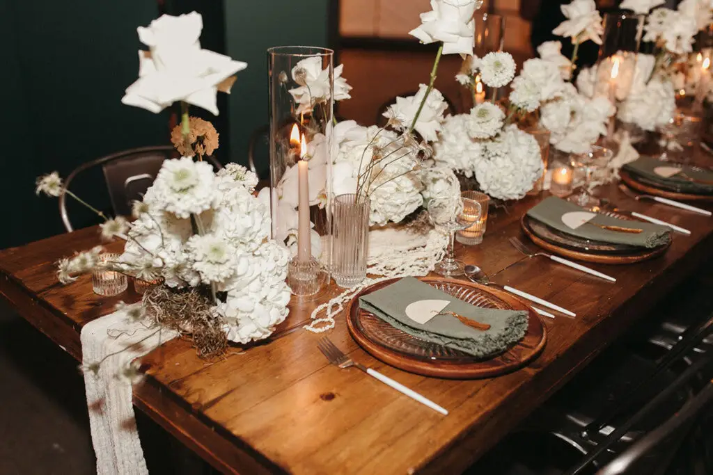 Wooden wedding table setup at Radius Indianapolis featuring white floral arrangements, tall candle centerpieces, and sage green napkins for weddings and celebrations.