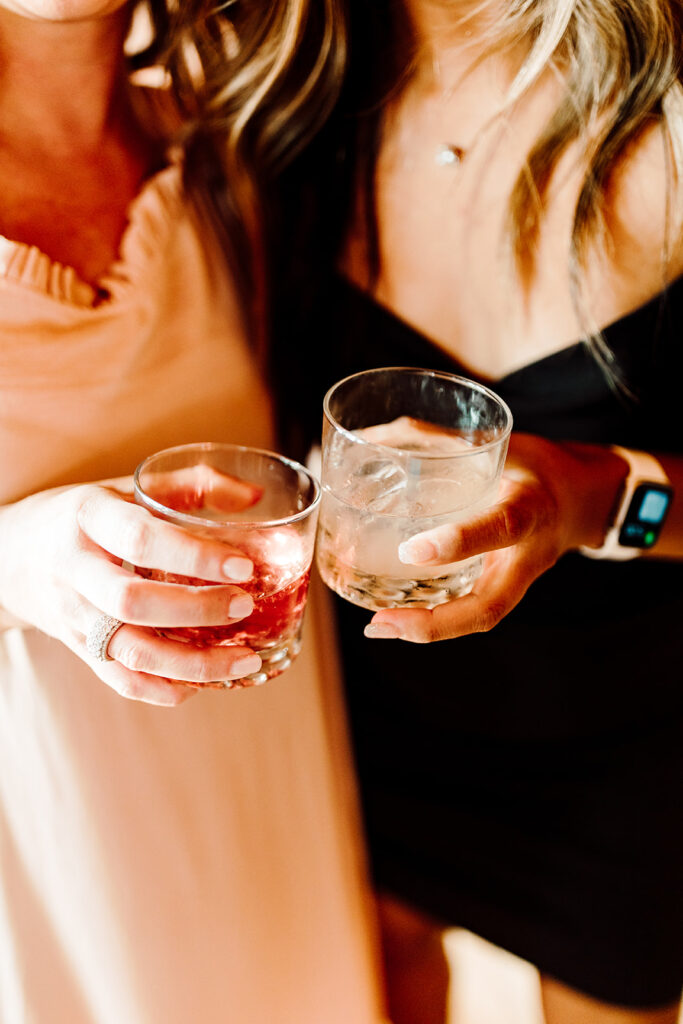 Two people's hands holding and clinking glasses of cocktails, celebrating at a party or wedding event.