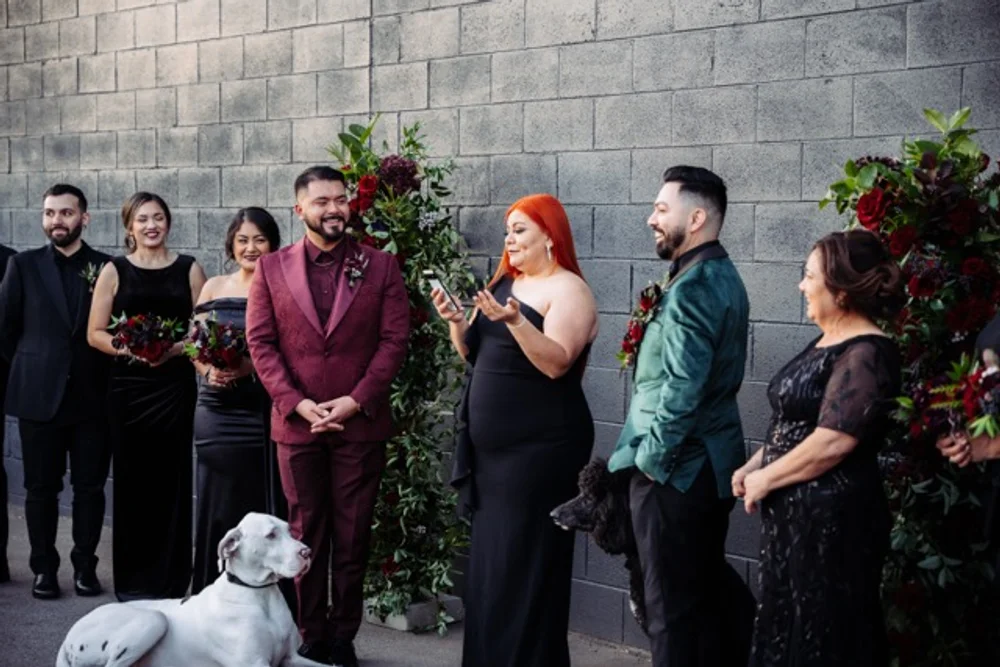 Two grooms, their wedding party and two dogs, standing outside during their wedding ceremony at dog-friendly event venue.
