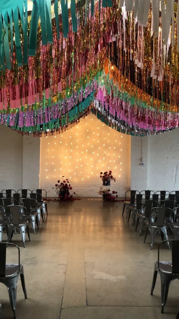 Wedding ceremony with twinkle lights, small florals, and a large hanging installation of streamers