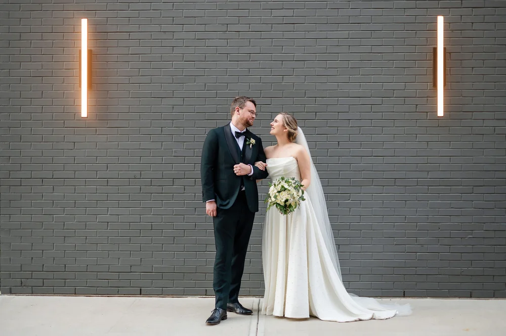 Bride and groom outdoors in front of gray brick wall
