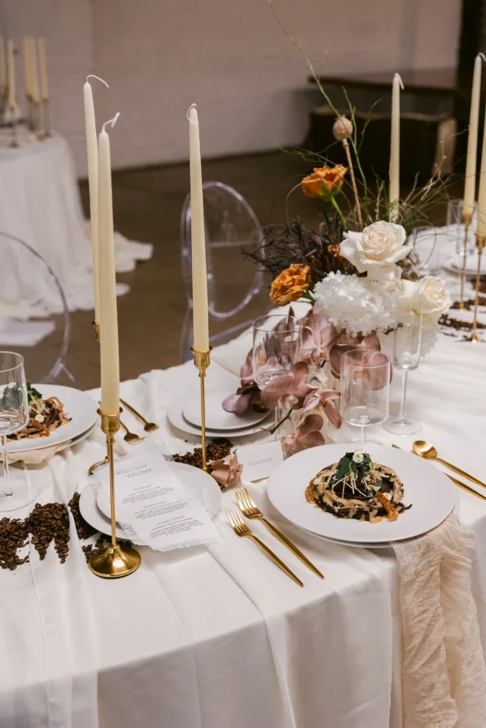 Curved wedding table with white plates and gold cutlery, plus candles, coffee beans and loose florals as the centerpieces at Indianapolis wedding venue.