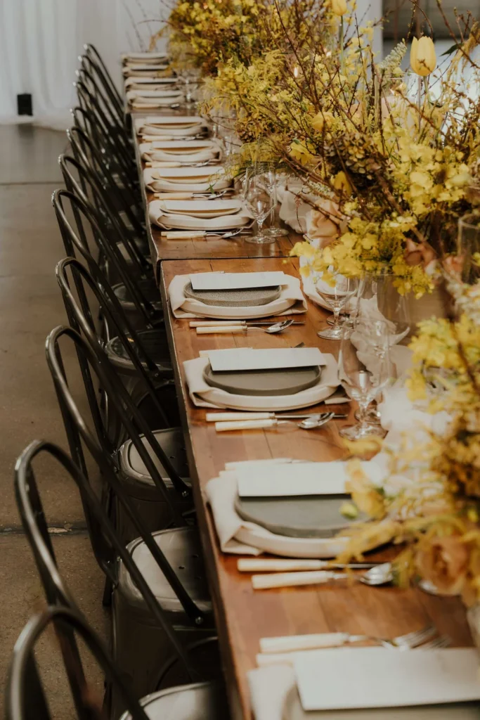 Long wooden table with matte cream and gray plates, yellow florals, and silver metal chairs at Radius Indianapolis.