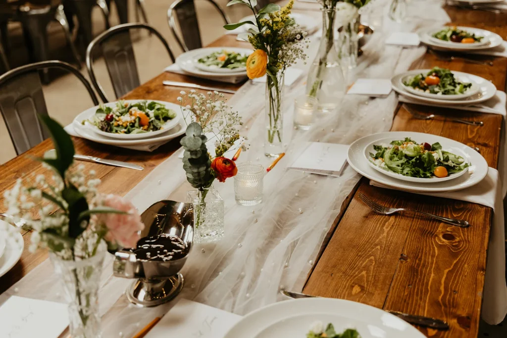 Wedding reception table with preset salads. a white table runner, and small bud vases with florals