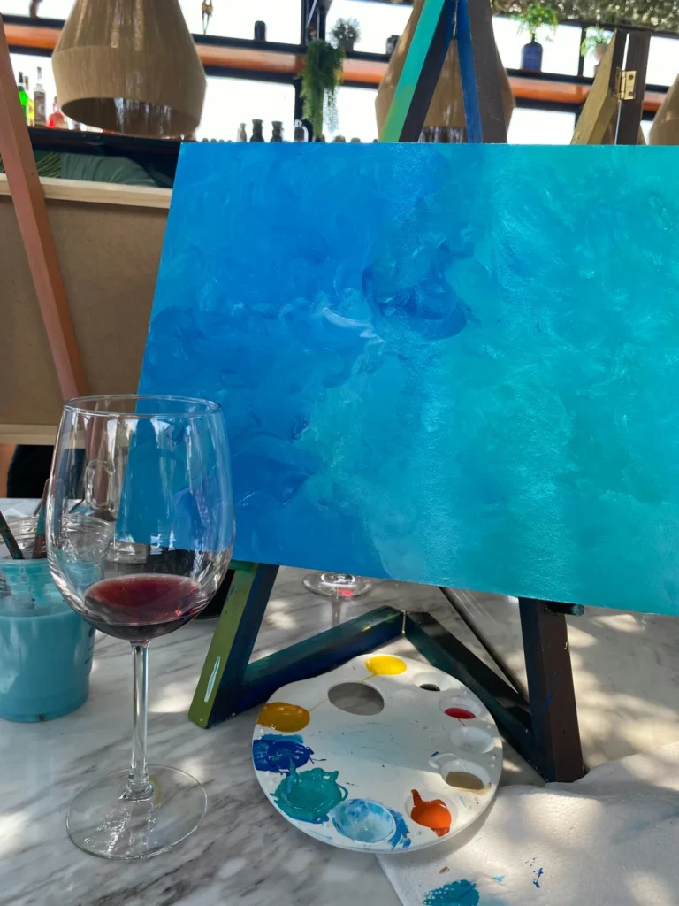 A canvas painted in different shades of blue, with a wine glass in front of it for a paint and sip team-building event.