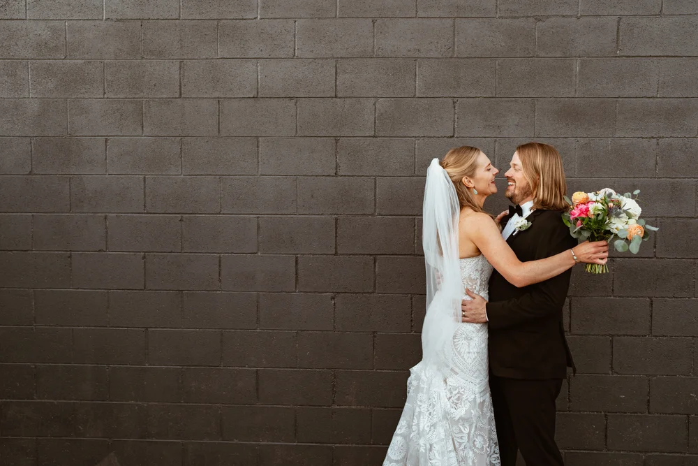 Bride and groom posing for a photo against Radius' outdoor gray brick wall