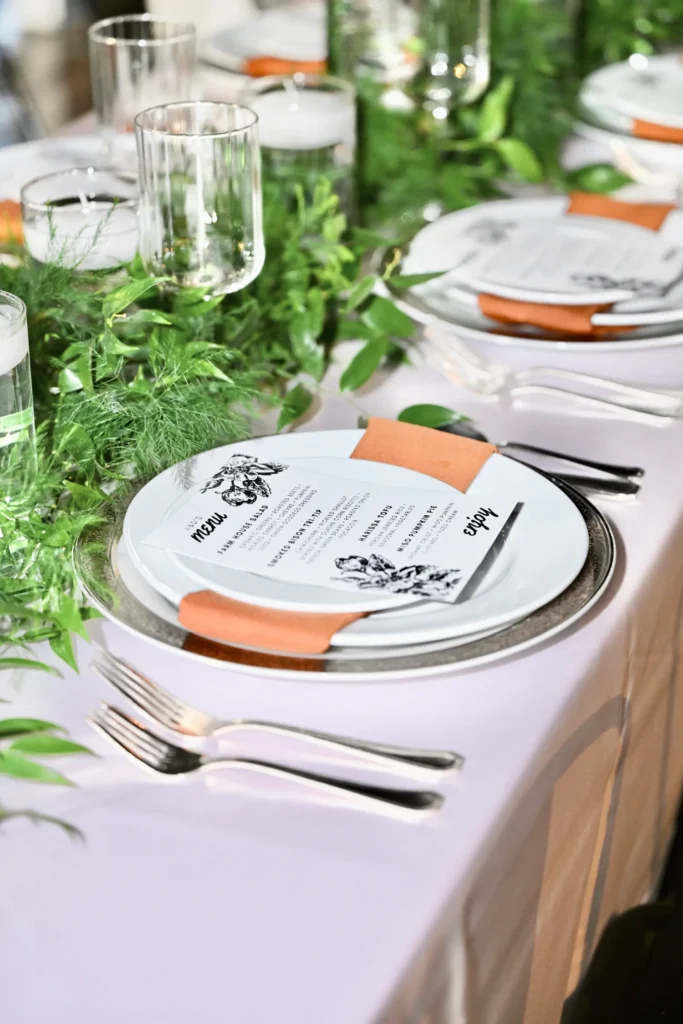 Reception table setup with greenery runner and orange napkins at an Indianapolis fundraising event.