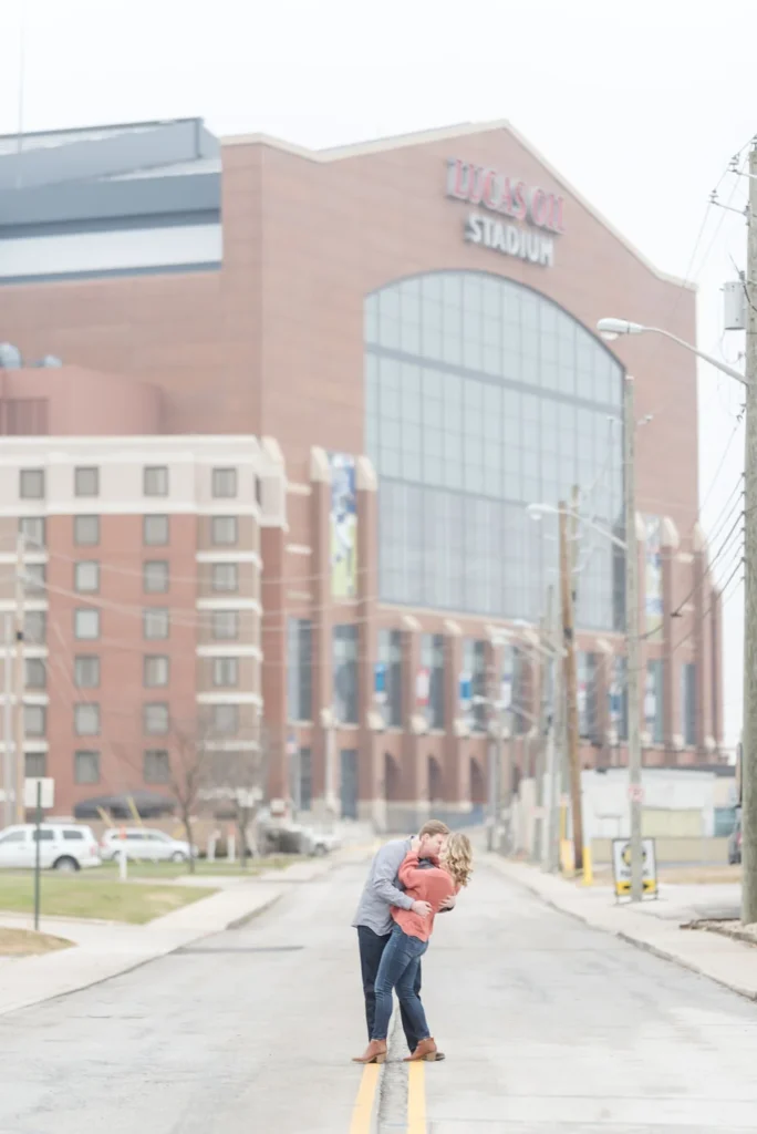 Couple posing for engagement photos in front of Lucas Oil Stadium in Indianapolis, IN
