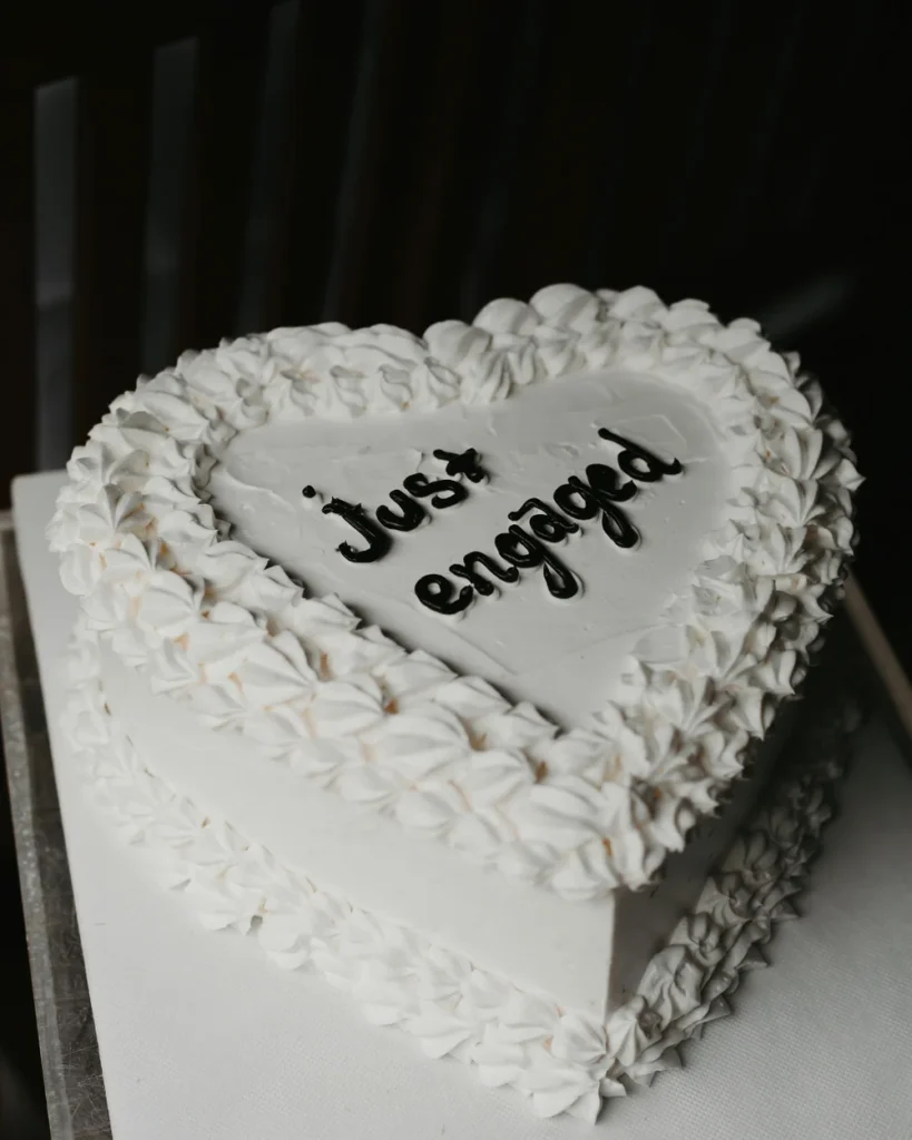 Heart-shaped white cake that reads 'just engaged' in black icing