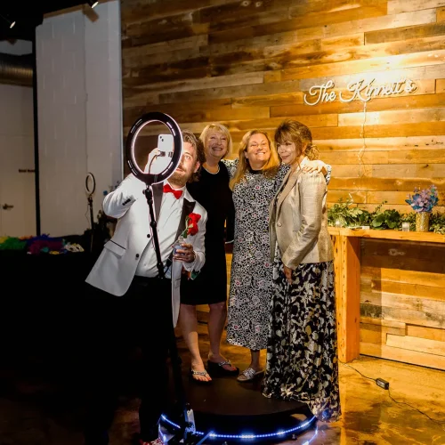 Wedding guests posing for a 360-degree photo booth at Radius, an event and wedding venue in Indianapolis, with a rustic wooden backdrop.